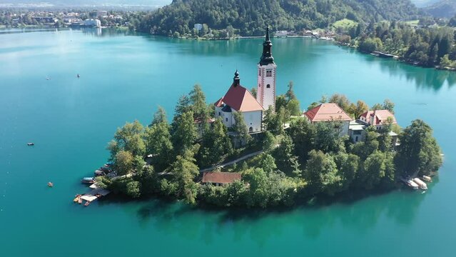 Church of the Assumption of Mary in the center of the lake Bled. Slovenia. Aerial. Summer. Drone video. Flying around small island on Bled Lake. Blue water and forest around.