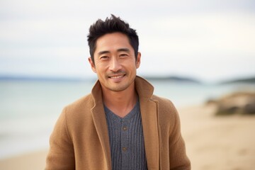 Medium shot portrait of a Chinese man in his 30s in a beach background wearing a chic cardigan