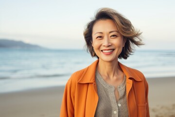 Medium shot portrait of a Chinese woman in her 50s in a beach background wearing a chic cardigan