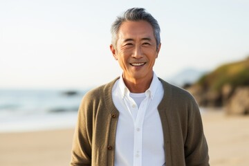 Medium shot portrait of a Chinese man in his 50s in a beach background wearing a chic cardigan