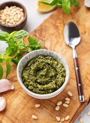 Traditional Italian pesto with green basil, pine nuts, cheese and olive oil on wooden board close up. A classic sauce for spaghetti or bruschetta.
