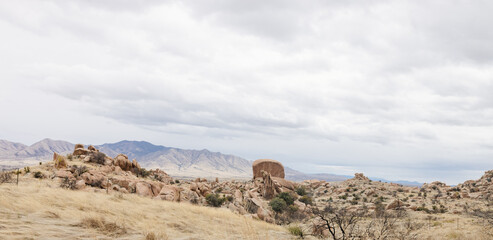 A beautiful landscape with a meadow with dry grass, bushes, large rocks and blue mountains in the background. Scenic American landscape on a cloudy autumn day