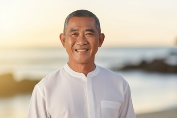 Medium shot portrait of a Indonesian man in his 60s in a beach background wearing a simple tunic