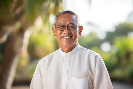Medium shot portrait of a Indonesian man in his 60s in a beach background wearing a simple tunic