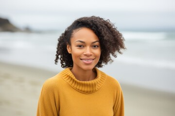 Lifestyle portrait of a Nigerian woman in her 20s in a beach background wearing a cozy sweater