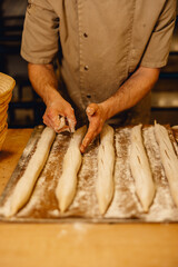 baker cuts top of unbaked baguettes with bread lame before they go in the oven in professional bakery