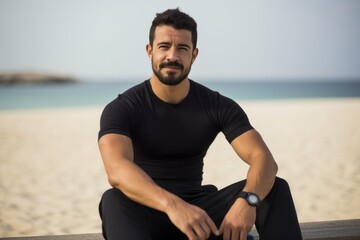 Fototapeta premium Portrait of a young man sitting on the beach looking at camera