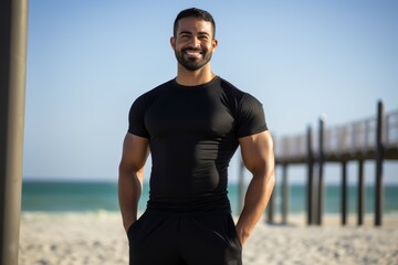 Portrait of smiling young man standing with hands on hips at beach