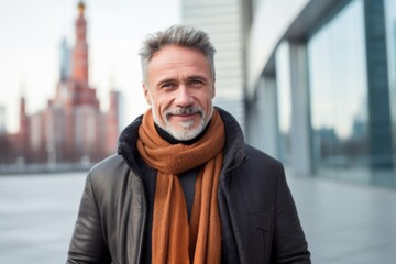 Handsome middle-aged man with grey hair and beard in a black jacket and orange scarf in the city