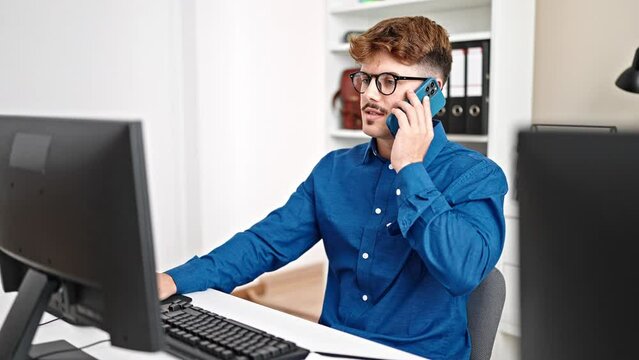 Young hispanic man business worker using computer talking on smartphone at the office