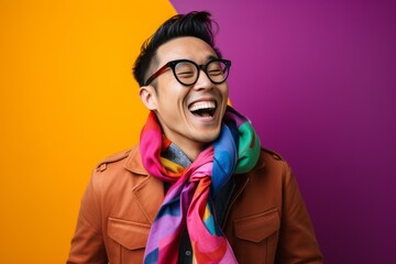 Fototapeta premium excited young asian man in coat and glasses laughing on colorful background