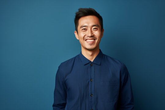 Portrait of a happy young asian man smiling against blue background