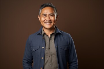 Fototapeta premium Portrait of happy mature Indian man smiling at camera against brown background