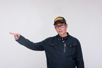 A serious asian male security guard points to the left with his finger. Directing or advising someone. Isolated on a white background.