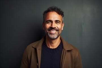 Portrait of a handsome Indian man smiling at the camera while standing against grey background
