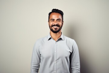 Obraz premium Portrait of a happy young bearded Indian man smiling against grey background