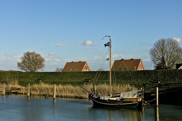 Naklejka premium Scenic view of a small boat docked along the bank of a canal. Hooksiel, Germany, North Sea.
