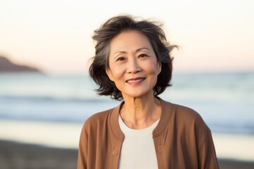 Portrait of a smiling senior woman standing on the beach at sunset