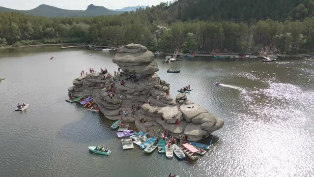 Boat trip on catamarans and boats.Stone island of Zhumbaktas in the middle of a mountain lake in Kazakhstan Borovoe.The rock in the middle of the water the Kazakh Sphinx.A lot of people on the water