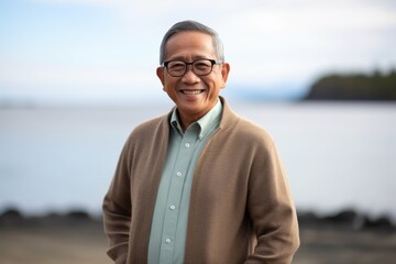 Fototapeta premium Portrait of happy senior asian man wearing glasses smiling at camera with sea in background