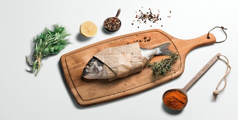 Close-up image of a fish wrapped in newspaper placed on top of a wooden cutting board