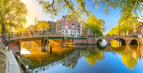 Panoramic view of Amsterdam in the morning sun. Traditional old houses, bridges and mirror water with reflection. Beautiful morning in Amsterdam. - 636749312