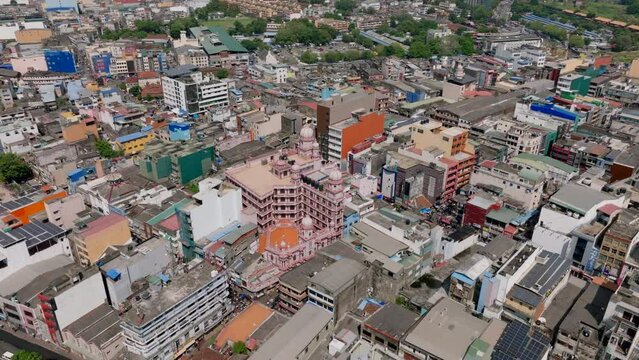 Aerial slide and pan footage of pink multistorey building, Jami Ul Alfar Mosque surrounded by buildings in urban borough. Colombo, Sri Lanka