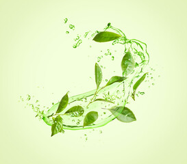 Fototapeta na wymiar Splashes of refreshing drink with leaves on pale green background. Green or matcha tea