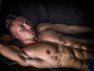 Photo of a shirtless man relaxing on a black sheets bed