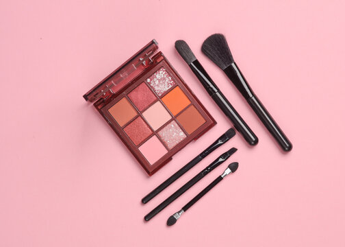 Eye shadow palette with makeup brushes on pink background. Beauty concept