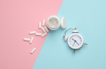 Pills bottle with alarm clock on a blue-pink background. Top view