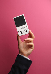 March 20 wooden block calendar in male hand on pink background