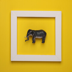 Toy elephant in white frame on yellow background. Creative layout. Minimalism