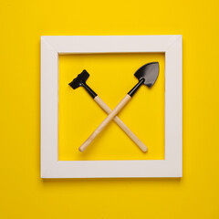 Miniature shovel with rake in white frame on yellow background. Creative layout. Minimalism