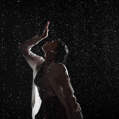 Dancing in the rain. A young woman in wet clothes dancing among water droplets, photo in the aqua studio. beautiful silhouette, model in a white shirt