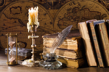 Antique table with old map, books, quill pen, candle, sandwatch. Vintage still life. Retro style.