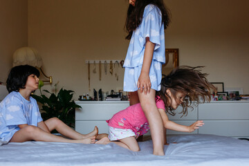Obraz na płótnie Canvas three little girls with dark hair playing on parents bed