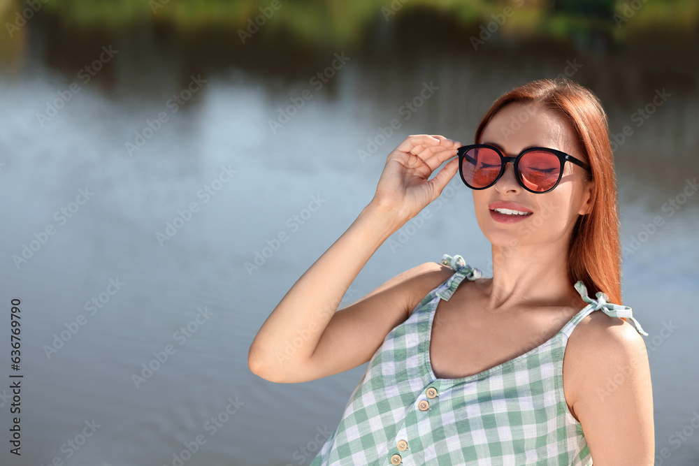 Sticker Beautiful woman in sunglasses near river, space for text