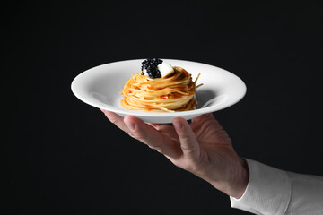 Waiter holding plate of tasty spaghetti with tomato sauce and black caviar on dark background,...