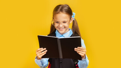Cheerful Schoolgirl Reading notebook Learning Over Yellow Background In Studio. School Education Concept