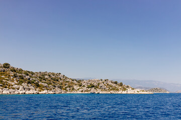Fototapeta na wymiar Beautiful view of the Mediterranean Sea with yachts. Picturesque landscape of blue ocean and green mountains on a sunny summer day. The sunken city of Kekova, Türkiye - 28 July 2023