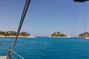 The Mediterranean Sea, surrounded by mountains, with picturesque islands in Turkey on sunny day. Summer background with blue ocean. People swim in the lagoon from a ship. Bodrum, Turkey - 28 July 2023