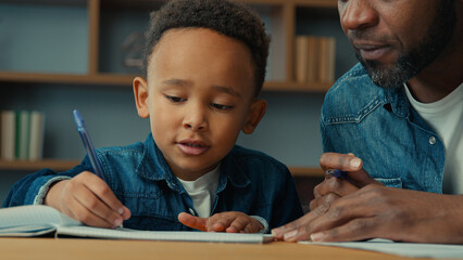 African American cute little boy child schoolboy with ethnic adult father writing homework. Dad help son with lesson class write explain exercise task kid close ears homeschooling elementary education