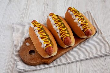 Char Grilled Hot Dog with Mustard, Relish and Onion on a rustic wooden board, side view.