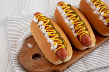 Char Grilled Hot Dog with Mustard, Relish and Onion on a rustic wooden board, side view.