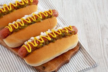 Char Grilled Hot Dog with Mustard, Relish and Onion on a rustic wooden board, side view.