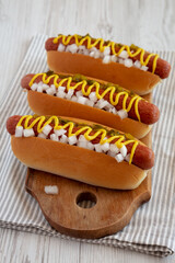 Char Grilled Hot Dog with Mustard, Relish and Onion on a rustic wooden board, side view.