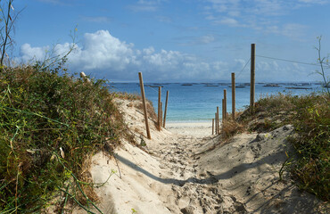 posts to protect an area of dunes on the beach with trays to cultivate mussels on the estuary in the background