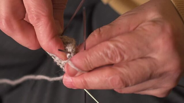an elderly woman knits on knitting needles close-up.