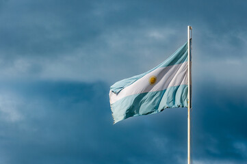 Light blue and white Argentinian flag waving with blue sky and grey clouds as background